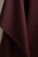 Gros plan sur le tissu coton déperlant bordeaux, drapé en plis souples avec une couture visible sur le bord.