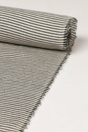 Gros plan sur le coin du tissu La Rayure 006 écru à fines rayures horizontales grises, mettant en valeur le motif et la lisière effilochée.