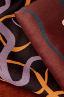 Pli du tissu montrant les deux faces : le motif graphique noir et lilas d'un côté, un uni bordeaux à liseré bleu-gris de l'autre.