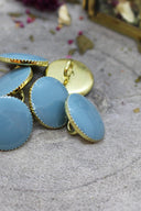 Gros plan rapproché sur les mêmes boutons Gem bleu gris facettés à liseré doré, sous un angle différent.