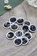 Gros plan sur les mêmes boutons émaillés cerclés de nacre, vue rapprochée révélant la texture brillante et le liseré blanc.