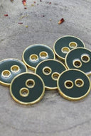 Cinq boutons ronds à deux trous, finition émaillée brillante vert cèdre foncé, cerclés d'un liseré métallique doré, posés sur une pierre grise avec des pétales de fleurs séchées éparpillés en arrière-plan.