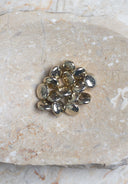 Boutons ronds bombés façon galet, finition métallique dorée brillante et réfléchissante, présentés en tas sur une pierre beige marbrée.