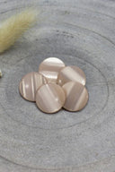Domed round shank buttons with no visible holes, pale pearly blush pink finish, piled on grey stone, with a sprig of dried grass in the background.