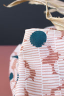 Gros plan sur le tissu Mirage écru, détaillant les pois marine et les taches terracotta sur fond rayé, avec une feuille séchée en arrière-plan.