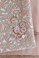 Tissu Petal écru plié, avec des boutons rose poudré et nacrés dispersés sur le motif de feuilles.