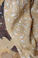 Tissu Petal moutarde plié, posé sur un plateau en bois avec des feuilles d'automne séchées à proximité.