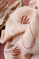 Gros plan sur le tissu Sandstorm rose poudré, détaillant les feuilles terracotta brodées et les contours graphiques du motif.