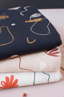 Tissus Sandstorm marine, rose poudré et écru pliés ensemble, montrant le même motif de formes abstraites dans trois coloris de la collection.