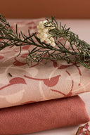 Tissu Windy rose poudré plié avec une branche de romarin séché et de petites fleurs blanches posée dessus, laissant apparaître un coupon uni terracotta en dessous.