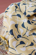 Tissu Windy moutarde drapé en plis souples, laissant apparaître l'ensemble du motif de feuilles courbes marine sur fond terracotta en arrière-plan.