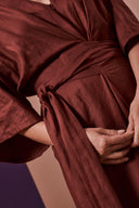 Patron La Combi Addie – Détail ceinture nouée, combinaison bordeaux, mains tenant les liens – Atelier Brunette