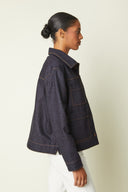 Patron Veste – vue de profil gauche, veste denim indigo coutures oranges, jean blanc – Atelier Brunette