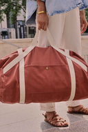 Patron Le Pack Escapade – Femme tenant le sac de voyage terracotta, anses écru, tenue décontractée – Atelier Brunette