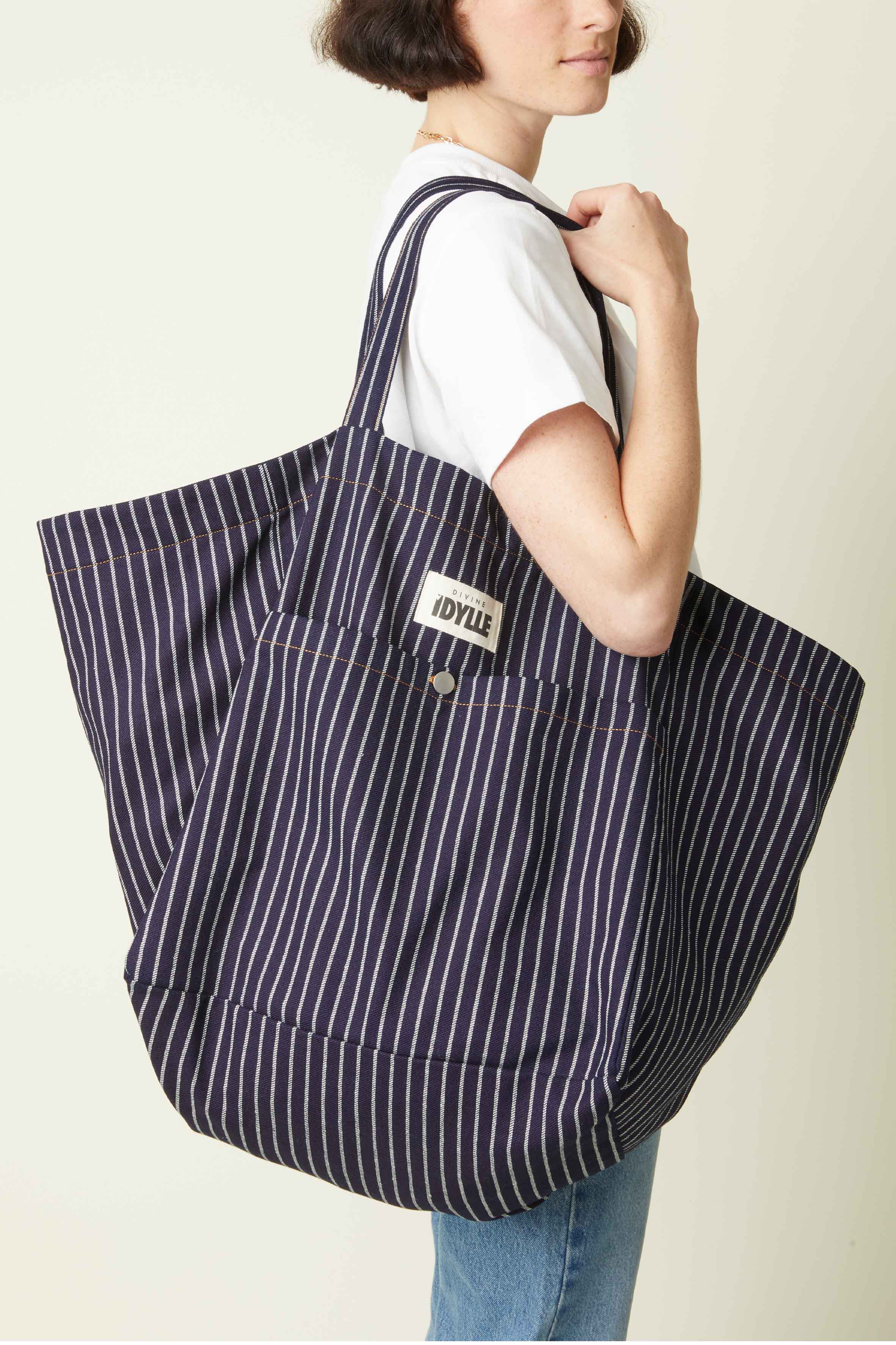 Patron Sac de plage – Femme de profil portant sac oversize rayé marine/blanc, anse épaule, fond beige – Atelier Brunette