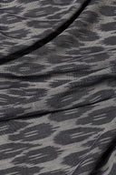 L'Ikat fabric in anthracite and light grey with an abstract ikat-style pattern, draped in diagonal folds over sheer voile.