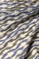 L'Ikat fabric in off-white with blue and anthracite ikat-style chevrons, draped in diagonal folds.