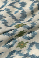 L'Ikat fabric in off-white with indigo blue ikat-style diamonds accented with olive green and orange touches, draped in soft folds.
