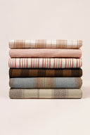 Stack of fabric remnants from the Le Bazaar collection, layered check and stripe patterns in khaki, navy, beige, dark green and brown tones.