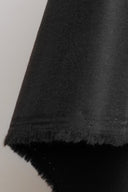 Close-up on the light black gabardine fabric, with the frayed selvedge visible on the folded edge.