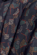 Tissu viscose Vera marine foncé à imprimé graphique pointillé sauge et terracotta, drapé avec des épis séchés en arrière-plan.